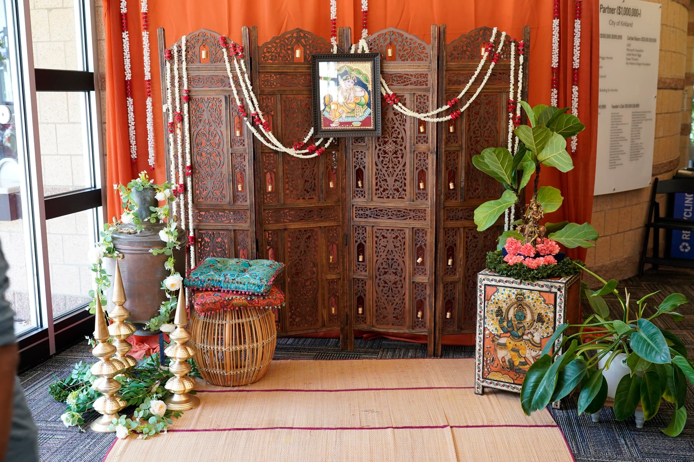 A hand-carved wooden screen backdrop with jasmine garlands, brass finials and cushions