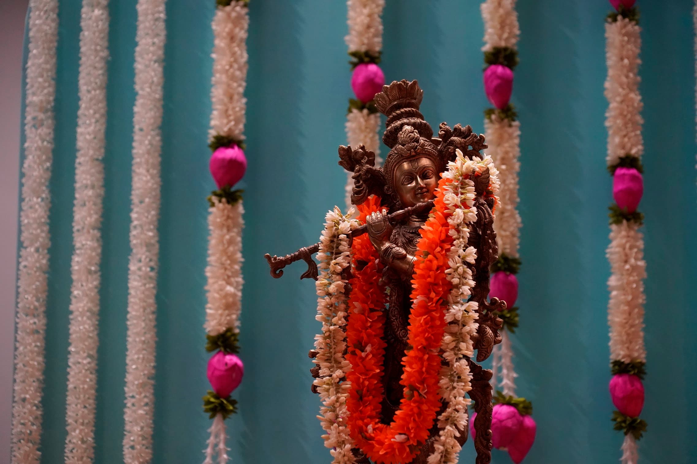 A garlanded brass murti against a teal drape, designed by Jayasri