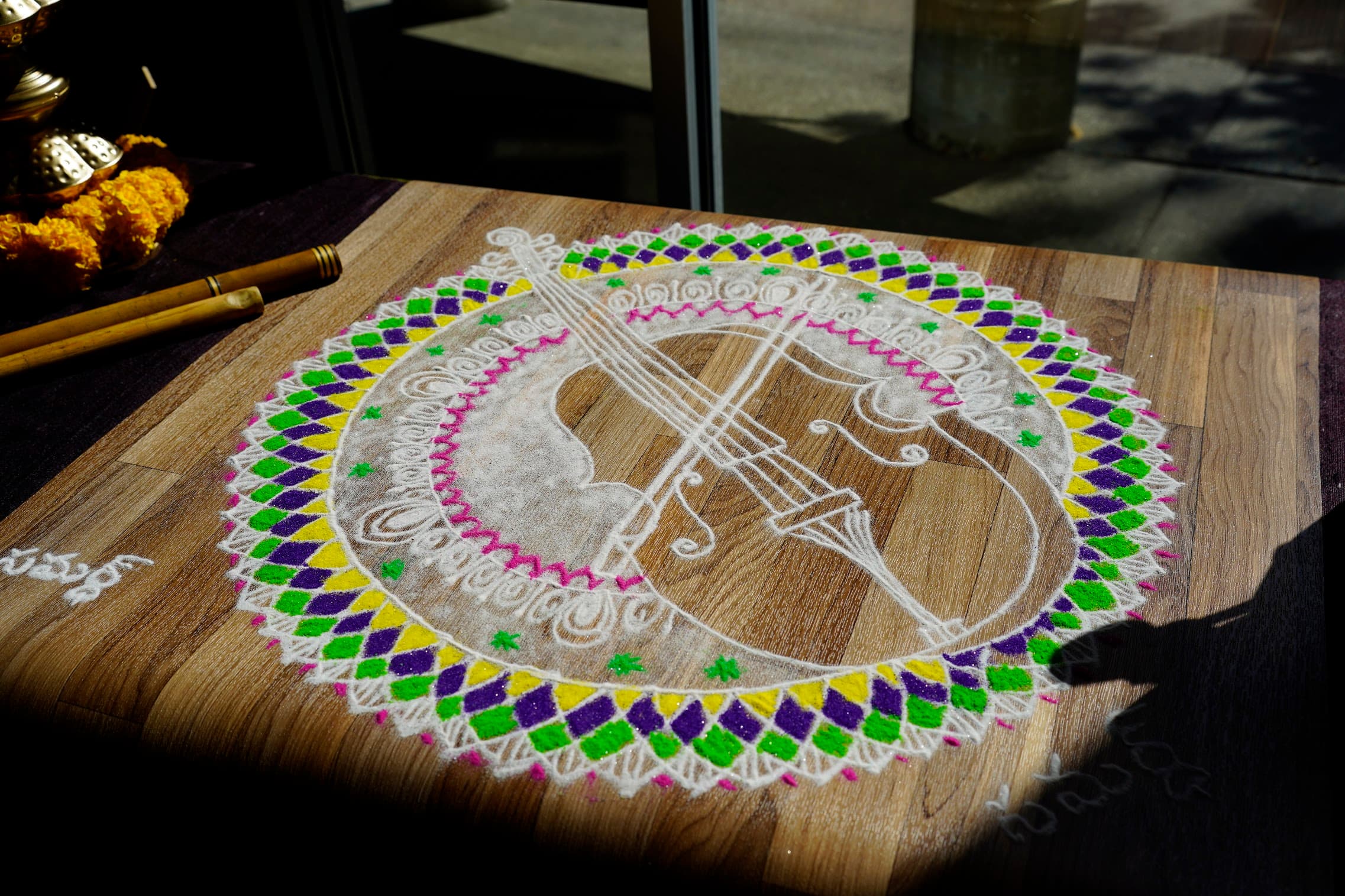 A hand-drawn violin rangoli in chalk and colour on a wooden floor
